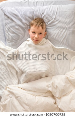 A emotional face of a blond boy in his bed covered by white blanket