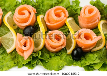 salmon snack on lettuce leaf with lemon and olives on white plate on white background