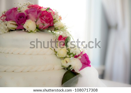 flower roses bouquet on top of white icing wedding cake with blurry bright background 