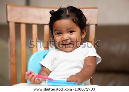 A surprised little girl holding a spoon and sitting in a high chair
