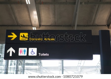 Domestic arrivals and toilets information board sign with yellow and white character on black background at international airport terminal.