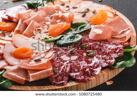 Antipasto platter cold meat, prosciutto, slices ham, beef jerky, salami, meat and nuts on cutting board over black stone background. Meat appetizer, catering food concept