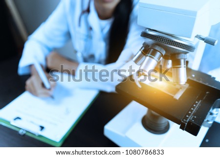 Female medical Doctor or research scientist looking through a microscope in a laboratory.science experiments,laboratory glassware containing chemical liquid for researching biology chemistry samples