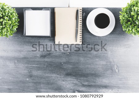 Close up of wooden office desk top with empty notepad, coffee cup and other items. Morning and document concept. Above view. Mock up