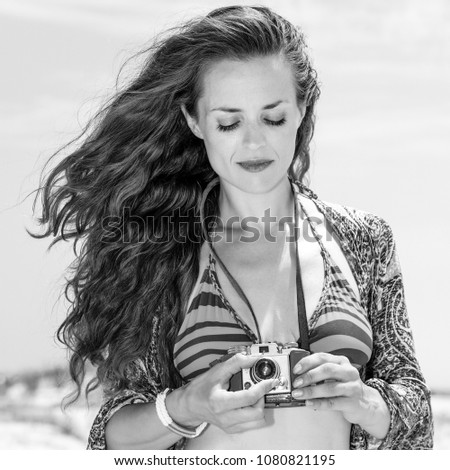 Bohemian vibe vacation. gypsy style young woman in swimsuit on the beach using retro photo camera