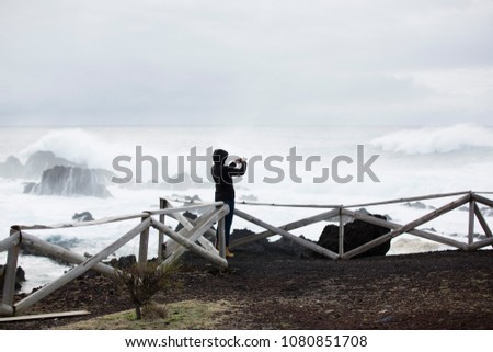 Wild, stormy weather, weavy ocean, rocky shore, wooden fence, woman in black look at the sea.