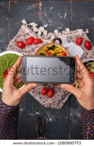 Woman hands take phone photo of food quinoa salad with fresh vegetables, pesto avocado dip sauce, tomatoes, seaweed, garlic. Smartphone photography of food for social media. Raw vegan vegetarian food.