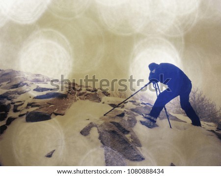 Abstract effect.  Travel photographer doing pictures in ancient stones on snowy peak of mountain. Winter cold and misty morning in mountains