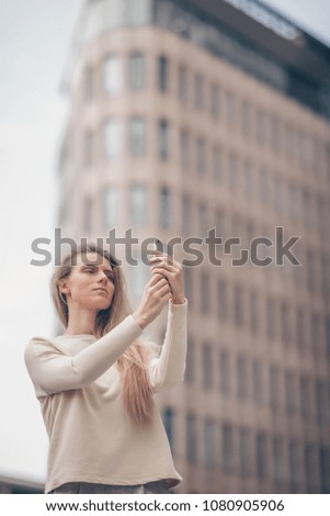 Beautiful woman is making a picture using a mobile phone near modern office building