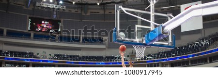 A basketball player's hand throws the ball into the basket. In the background there is a large LED information board Royalty-Free Stock Photo #1080917945