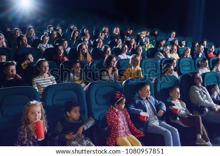 Crowd of people sitting in comfortable seats in modern movie theatre. Children, teens, adults watching  film and sipping fizzy drinks. Concept of cinematography and entertainment.