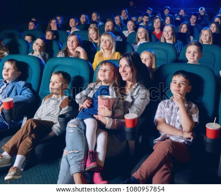 Children, teens, adults watching film with steadfast eyes in modern movie theatre. Smiling viewers eating snacks, sitting in comfortable chairs. Concept of cinematography and entertainment.