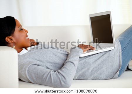 Portrait of a young relaxed woman working on laptop while is lying on sofa at home