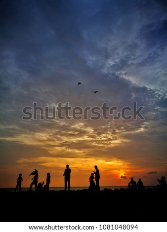 Silhouette of people spending their sunset activities along the beach. Among others playing kites and loafing. Selective focused and blurred motion of people and kites.