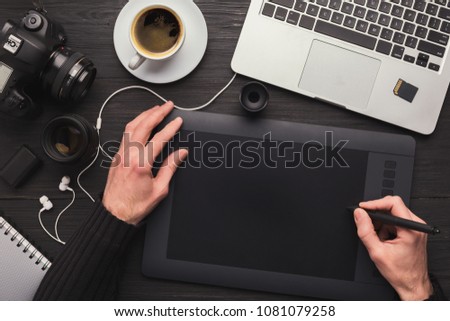 Top view on workplace of photographer. Creative designer hands working graphic tablet, photographic equipment on table