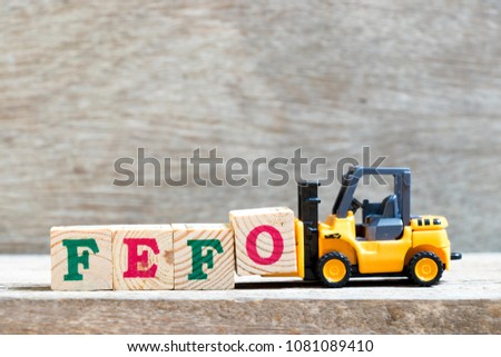 Toy forklift hold letter block O to complete word FEFO (first expired first out) on wood background