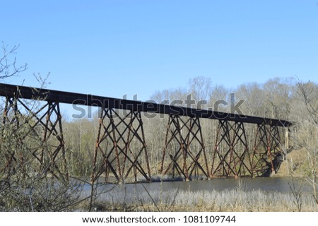 Rural landscape photo of an old rusty train bridge over a small lake in the woods