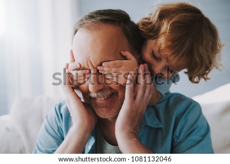 Small grandson closes with hands an eyes of grandfather. Guess Who Game. Royalty-Free Stock Photo #1081132046