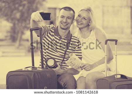portrait of young cheerful traveling couple taking self picture using mobile phone outdoors 

