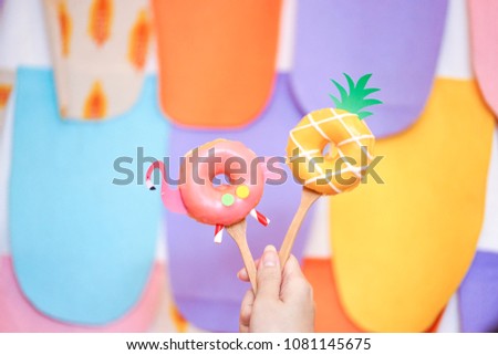Cute donuts. A lady's hand holding cute flamingo and pineapple sugar glazed doughnuts isolated on colorful background. Summer theme. Fancy food concept for birthday or creative party.