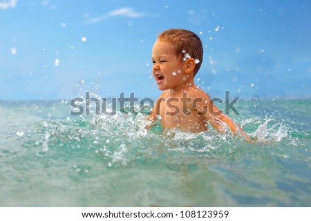 happy baby boy making water splashes in the sea