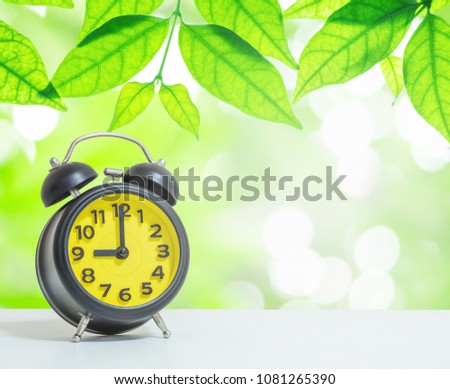 Closeup alarm clock show the time in 9 o'clock on white desk on blurred leaves in garden view in the morning textured background