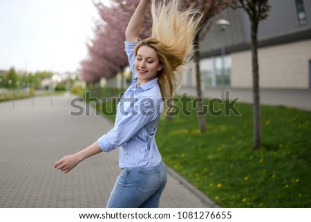 Young stylish woman wearing blue shirt, blue cropped denim jeans posing near blooming trees. Trendy casual outfit. Street fashion. Hair flip
