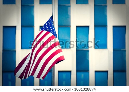 An American flag is waving on a blurred blue building full of windows in Manhattan, New York, United States.