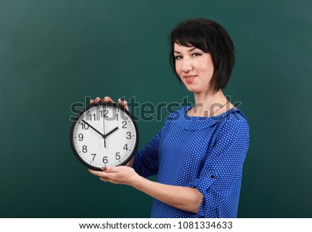 woman student with big clock posing by chalk Board, education concept, green background, studio shot