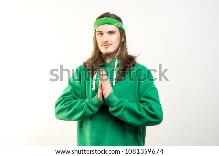 Portrait of young handsome man in green hoodie with a peaceful smile showing namaste agains white background. Lifestyle and people concept