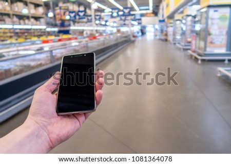 Hand holding mobile phone with shopping mall blurred background and bokeh light, Internet, Social medai. Hand with mobile phone on a background of a blurry shopping center
