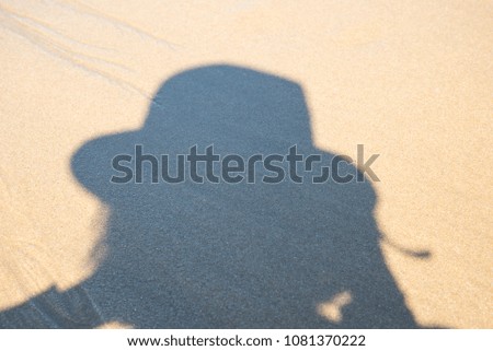 Shadow of women in hat taking photo on a beach