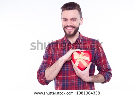 Portrait of an attractive smiling casual man giving present box and looking at camera isolated over white