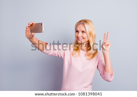 Portrait of charming stylish pretty cute trendy aged woman using cell smart phone shooting selfie on front camera gesturing v-sign two fingers isolated on grey background