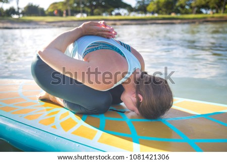 Sunny morning sun flare moment of a pretty young woman in SUP Yoga practice on a beautiful day