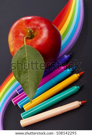 red apple, color paper and pencils on a black background
