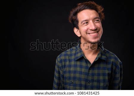 Studio shot of young Asian man wearing green checkered shirt against black background