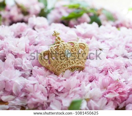 Gold crown. Queen or king. Green leafs. lur background. Gift for woman. Bright pink flowers on white painted wooden planks. Selective focus. Place for text.