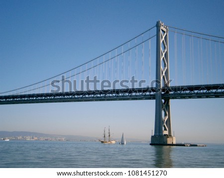 Boats sail under the San Francisco side of Bay Bridge with Oakland in the distance on a clear day.
