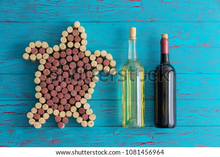 Creative artistic sea turtle formed of red and white wine bottle corks alongside unlabelled bottles of wine on a crackle paint turquoise wooden blue background
