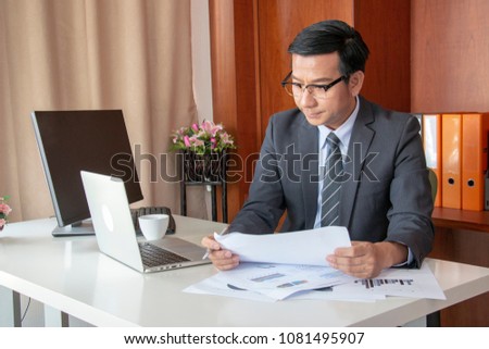 Businessman is working in the office. His desk got lots of data and computer and a cup of coffee