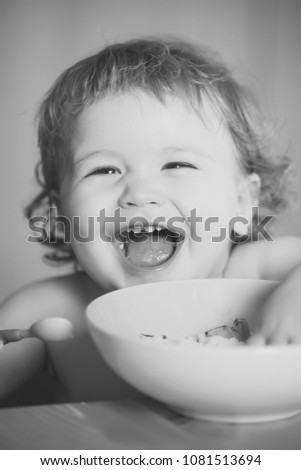 Portrait of funny little laughing baby boy with blonde curly hair and round cheecks eating from green plate closeup, vertical picture