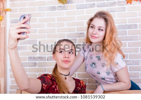 Two charming young girls take a selfie on the phone in a room furnished in autumn style