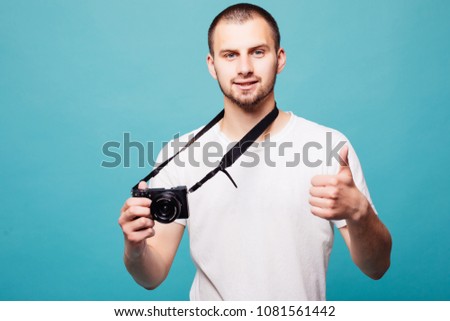 Picture of handsome emotional young man photographer isolated over blue wall background holding camera.