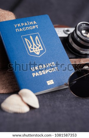 Ukrainian travel passport on gray background. sunglasses, hat. vintage camera on the background. EU visa free access. Shallow depth of field, focus on the Ukrainian logo on the passport.
