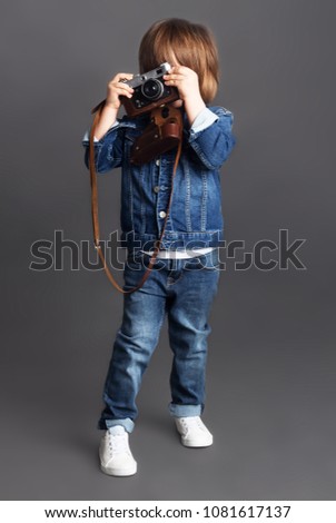 A little boy in denim tries to take a shoot using a vintage film camera.