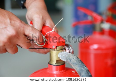 Hand pulling pin of fire extinguisher.