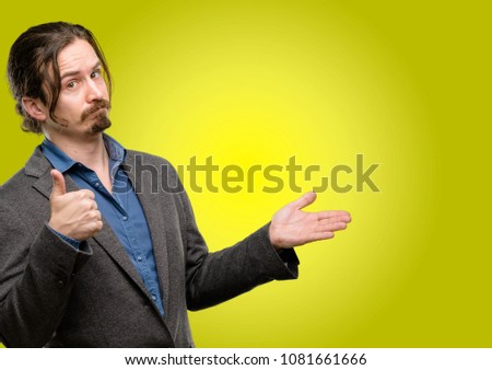 Handsome young man thumb up holding something in his empty hand and making ok gesture