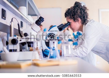 Young scientist looking through a microscope in a laboratory doing research Royalty-Free Stock Photo #1081663553