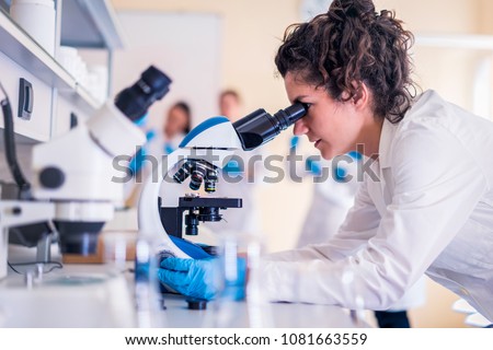Young scientist looking through a microscope in a laboratory doing research Royalty-Free Stock Photo #1081663559